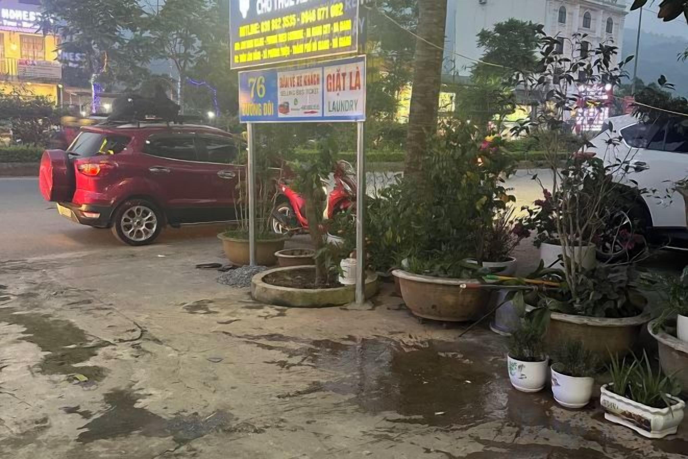 A street scene with a red SUV parked on the side, a motorcycle, and several potted plants.