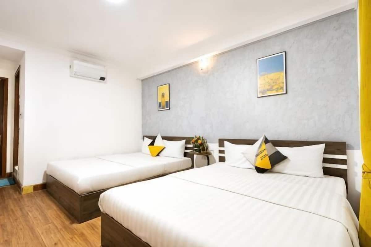 Une chambre d’hôtel avec deux lits, un plancher en bois, un mur gris et un tableau.