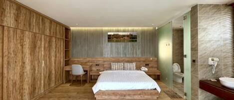 Un dormitorio con cama, escritorio, silla y baño con lavamanos y retrete.