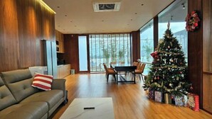 A modern living room with a sofa, a coffee table, a dining table with chairs, a Christmas tree, and large windows. - Villa SuSu (Da Nang)