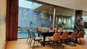A modern dining area with a large table and chairs, a view of a pool, and a brick wall with 'Villa SUSU2' signage. - Villa SuSu (Da Nang)