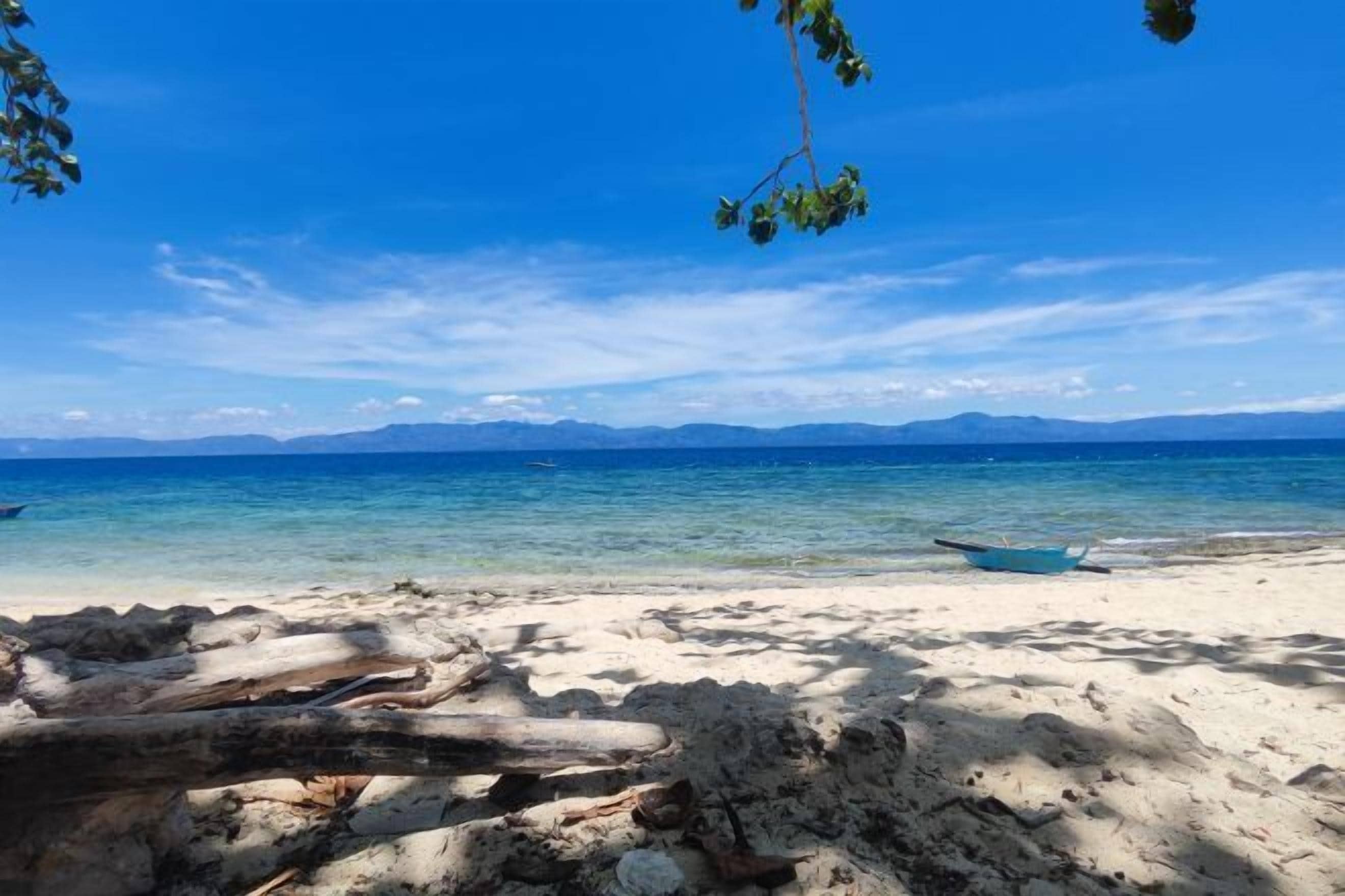 Uma praia com águas azul-claras, um barco na margem e montanhas ao longe.