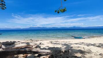 Uma praia com águas azul-claras, um barco na margem e montanhas ao longe.