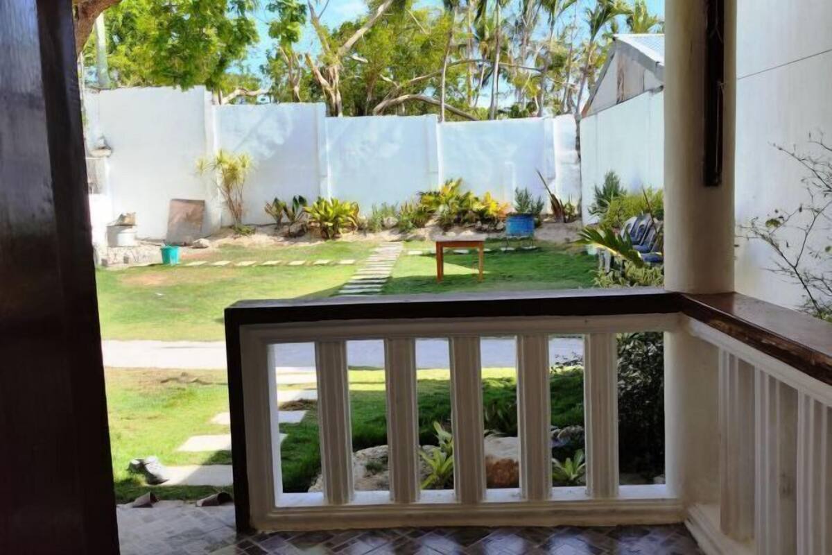 Blick vom Balkon mit weißer Brüstung, einem kleinen Tisch und einem Garten mit verschiedenen Pflanzen und einem Weg.