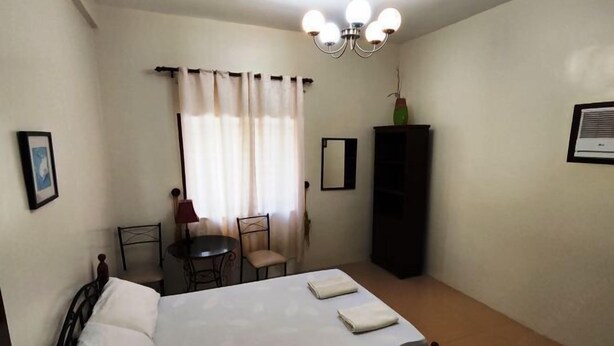 Ein Schlafzimmer mit einem Bett, einem Schreibtisch, zwei Stühlen, einem Schrank und einer Kandelaber.