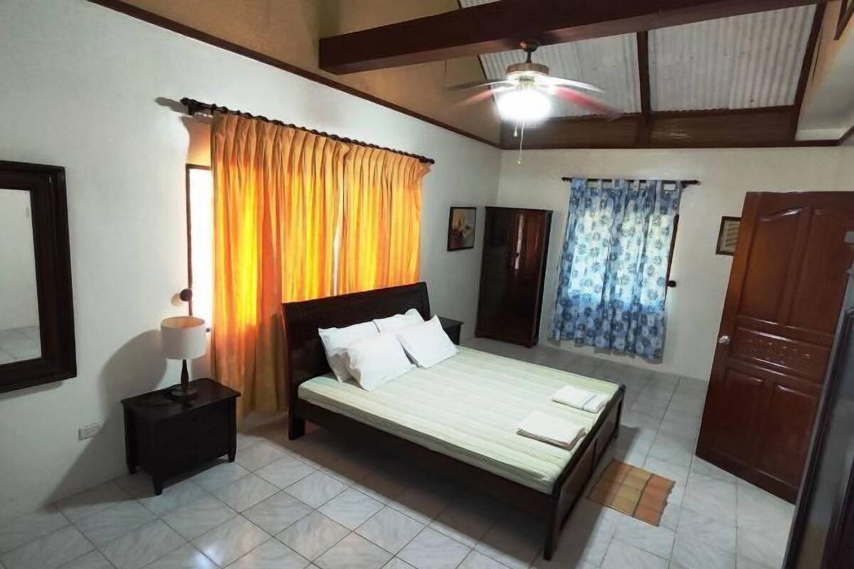Ein Schlafzimmer mit einem Bett, einem Nachttisch, einem Deckenventilator und Vorhängen.