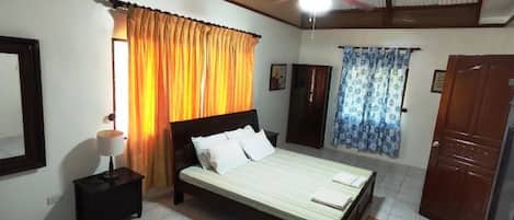 Une chambre à coucher avec un lit, une table de chevet, un ventilateur de plafond et des rideaux.