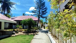 A pathway leading to a building with a red roof, surrounded by greenery and a bamboo fence. - Bluewaves Resort Moalboal by Hiverooms (Moalboal)