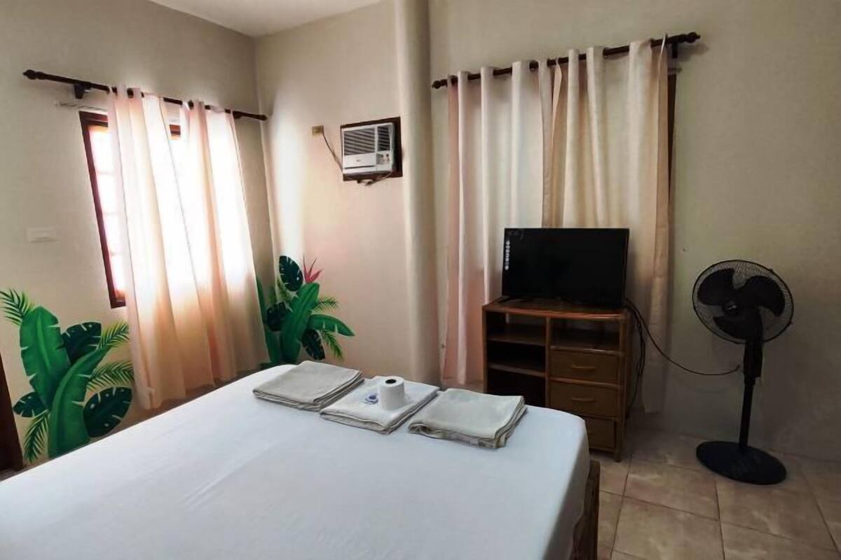 Ein Hotelzimmer mit einem Bett, einem Fernseher, einem Ventilator und einem Fenster mit Vorhängen.