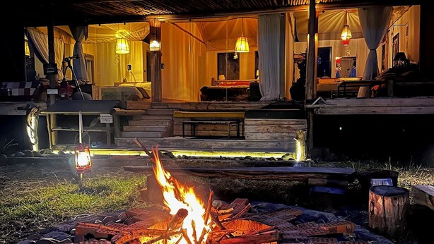 A cozy outdoor seating area with a fire pit, a covered patio, and a well-lit interior.