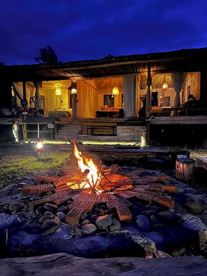 Un espacio al aire libre acogedor con una chimenea, un porche cubierto y un interior bien iluminado.