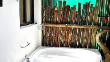 A bathroom with a large bathtub, a window, and a wooden fence.
