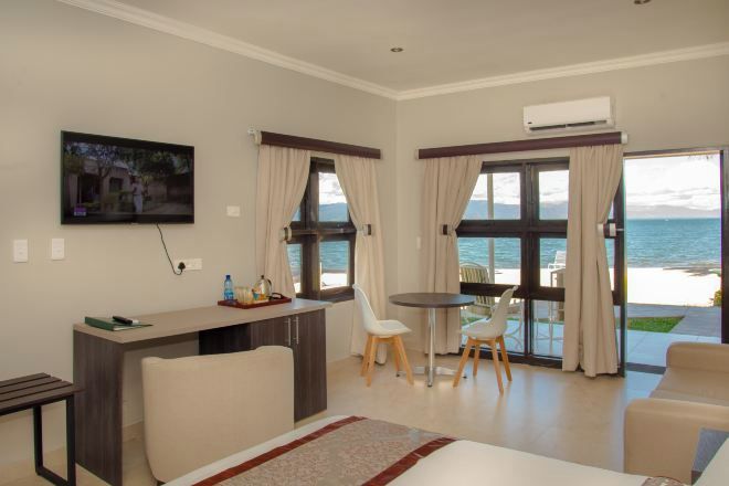 A modern hotel room with a bed, a desk, a chair, and a table. There is a TV mounted on the wall and a window with curtains.