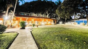 A hotel with a well-lit exterior, a paved pathway leading to the entrance, and a grassy lawn.