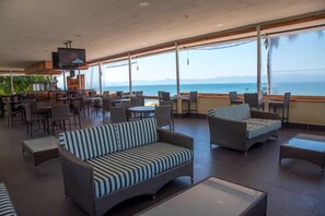 Un amplio espacio interior con mobiliario de mimbre, un televisor y vista al mar.