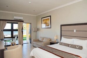A hotel room with a bed, a sofa, a desk, and a view of the sea. - Sunbird Nkopola (Mangochi)