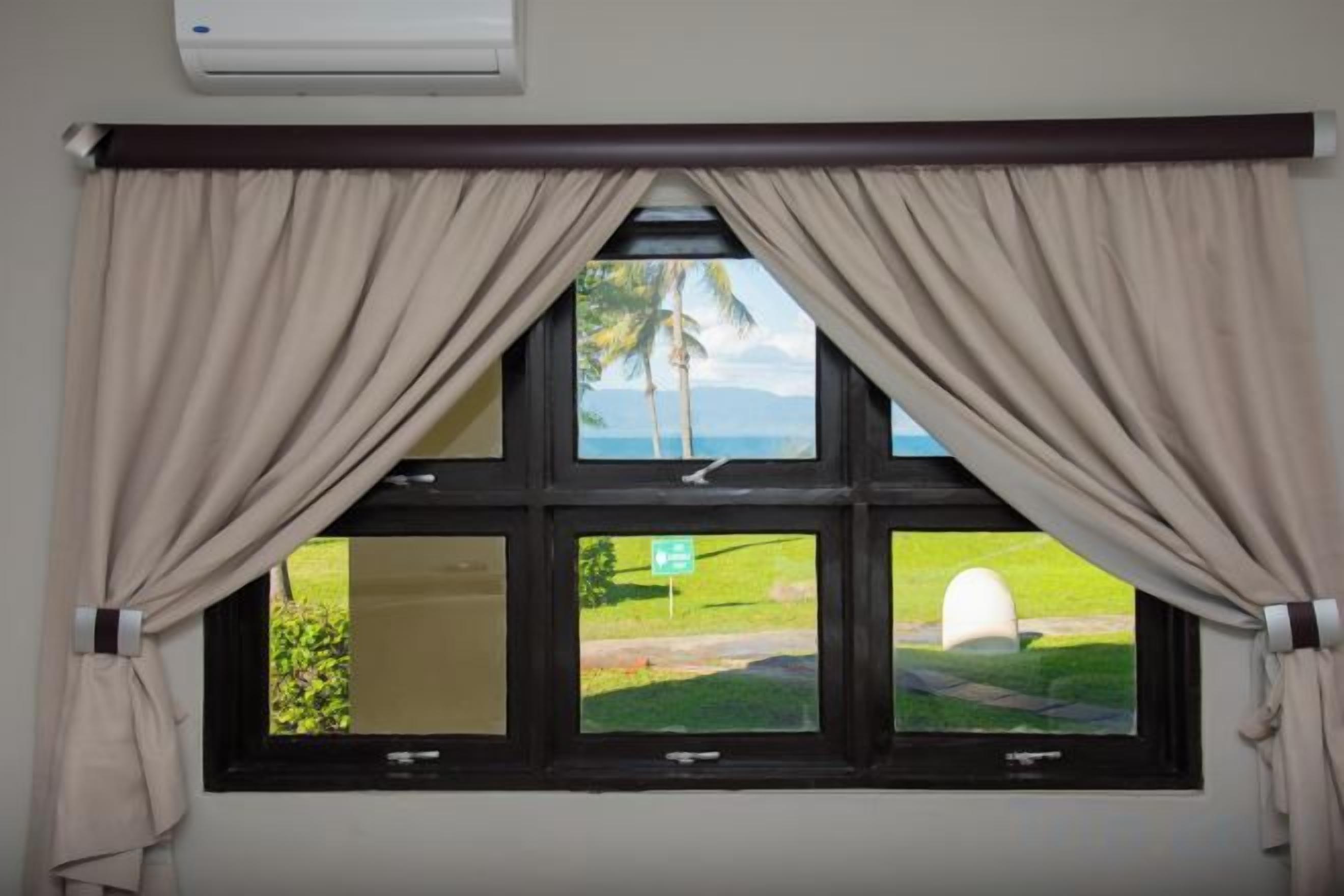 Uma janela com cortinas, vista para uma área gramada e uma palmeira.