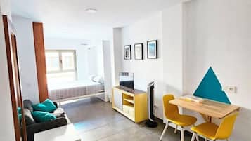 Ein modernes Wohnzimmer mit einer Couch, einem Esstisch mit Stühlen, einem Fernseher und einem Bett im Hintergrund.