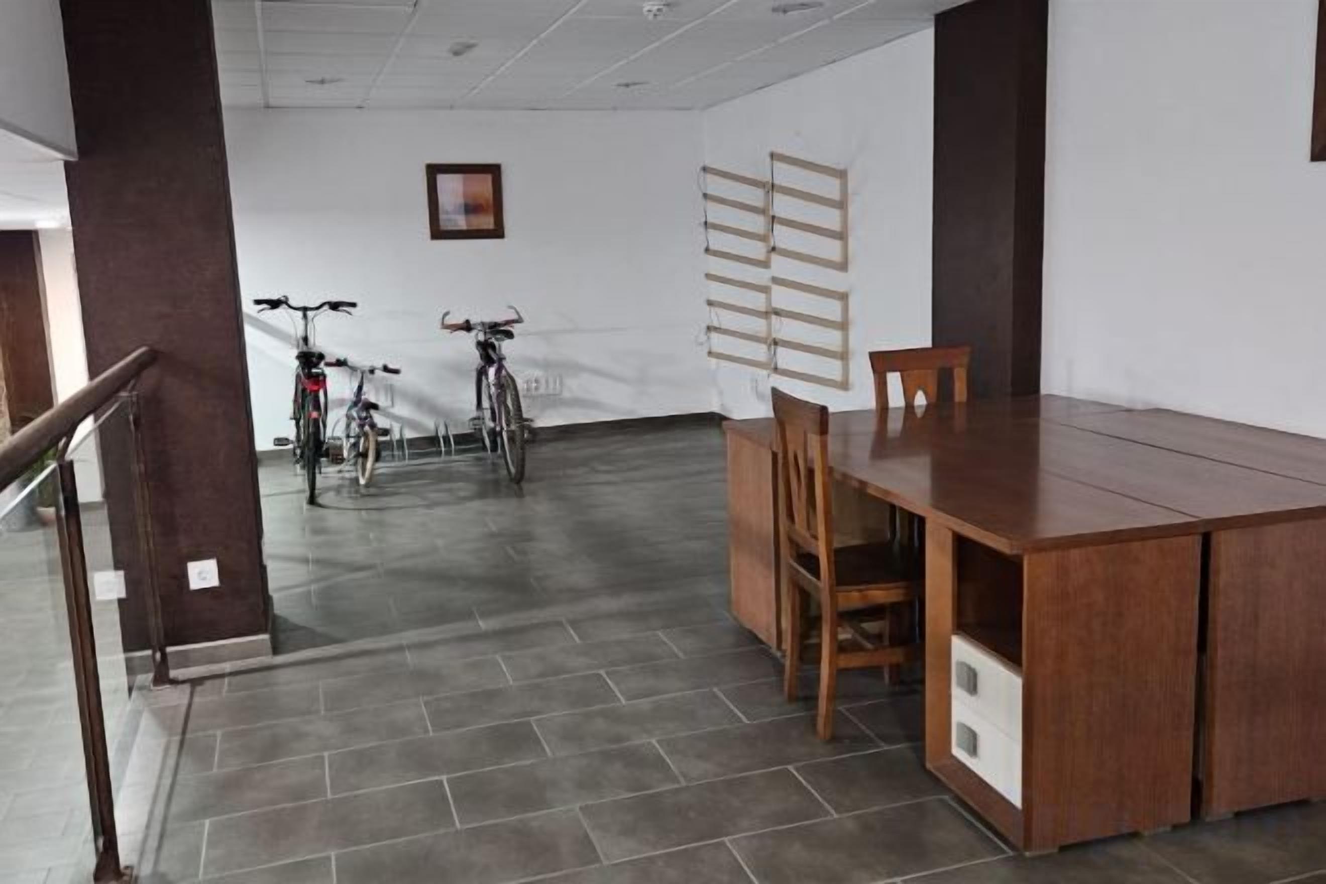 Quarto espaçoso com uma mesa de madeira e cadeiras, uma escada e bicicletas encostadas na parede.