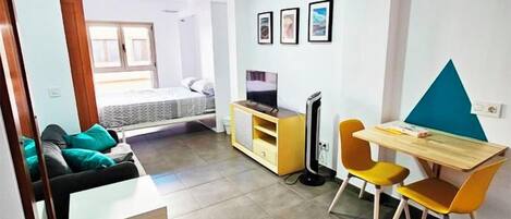 Een knus woongedeelte met een bed, een televisie, een bureau met stoel en een kleine kitchenette.