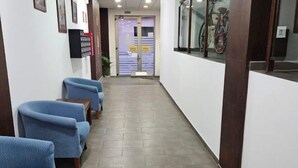 A hallway with blue chairs lined up on one side, a tiled floor, and a door at the end. - Lala Loft, Las Canteras (Las Palmas)