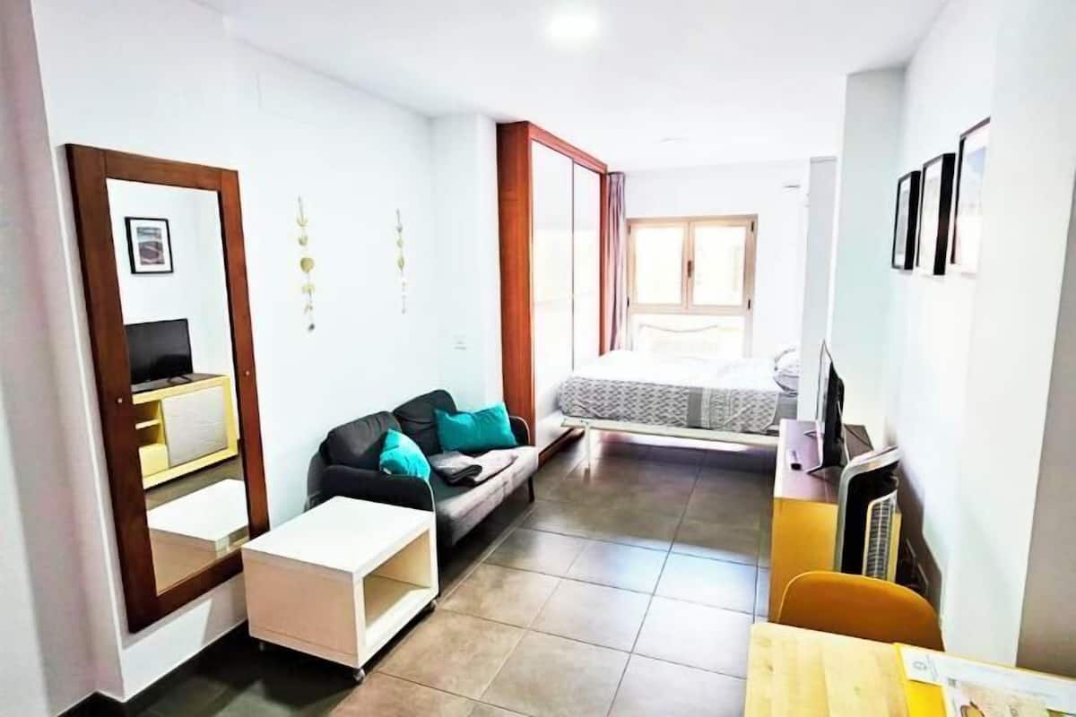 A compact living space with a sofa, a small table, a TV, and a bed.