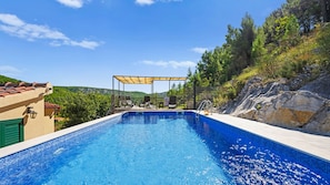 Une piscine agrémentée d’une pergola et de chaises longues, entourée de verdure et de collines.