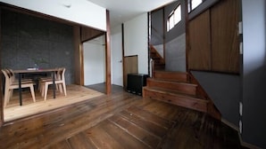 Un espacio amplio con piso de madera, una mesa de comedor con sillas, una escalera y una pared oscura.