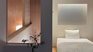 Una habitación con cama, mesita de noche, luz empotrada en la pared y ventana con vistas.