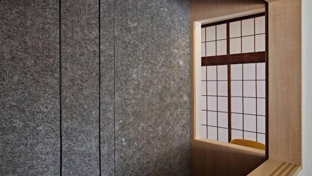 Una habitación con pared de piedra, ventana de madera con diseño de cuadrícula y un banco de madera.
