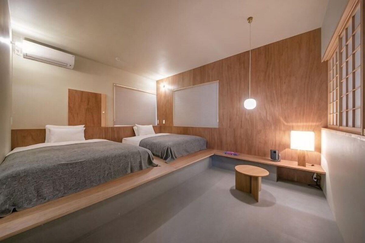 A hotel room with two beds, a small seating area, a wooden accent wall, and a hanging light fixture.