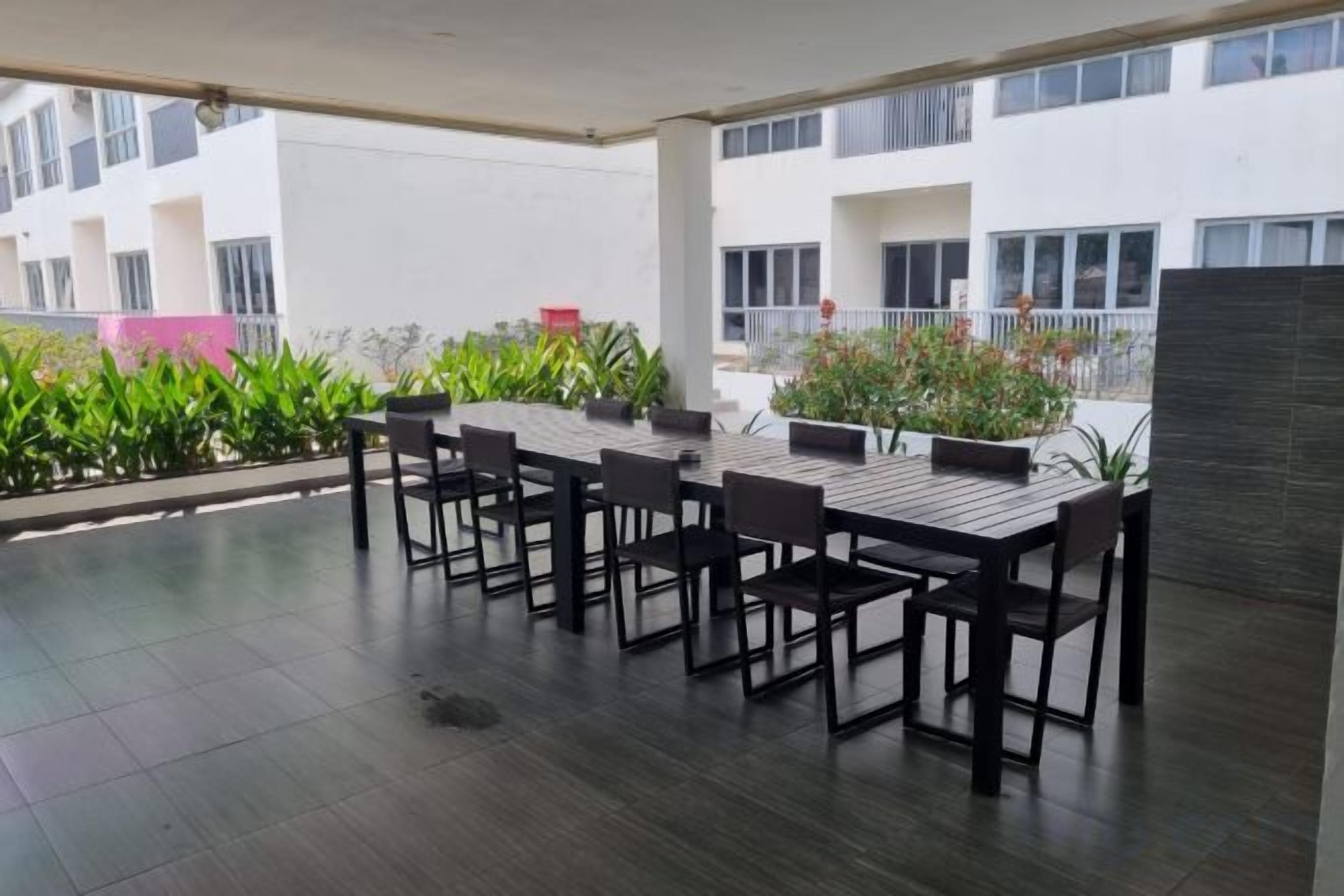 An outdoor patio with a table and chairs, surrounded by potted plants and a view of a building.