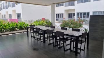 An outdoor patio with a table and chairs, surrounded by potted plants and a view of a building.