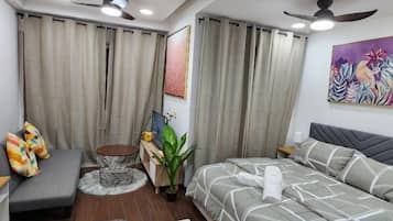 A modern bedroom with a bed, a sofa, a small table, and a ceiling fan.
