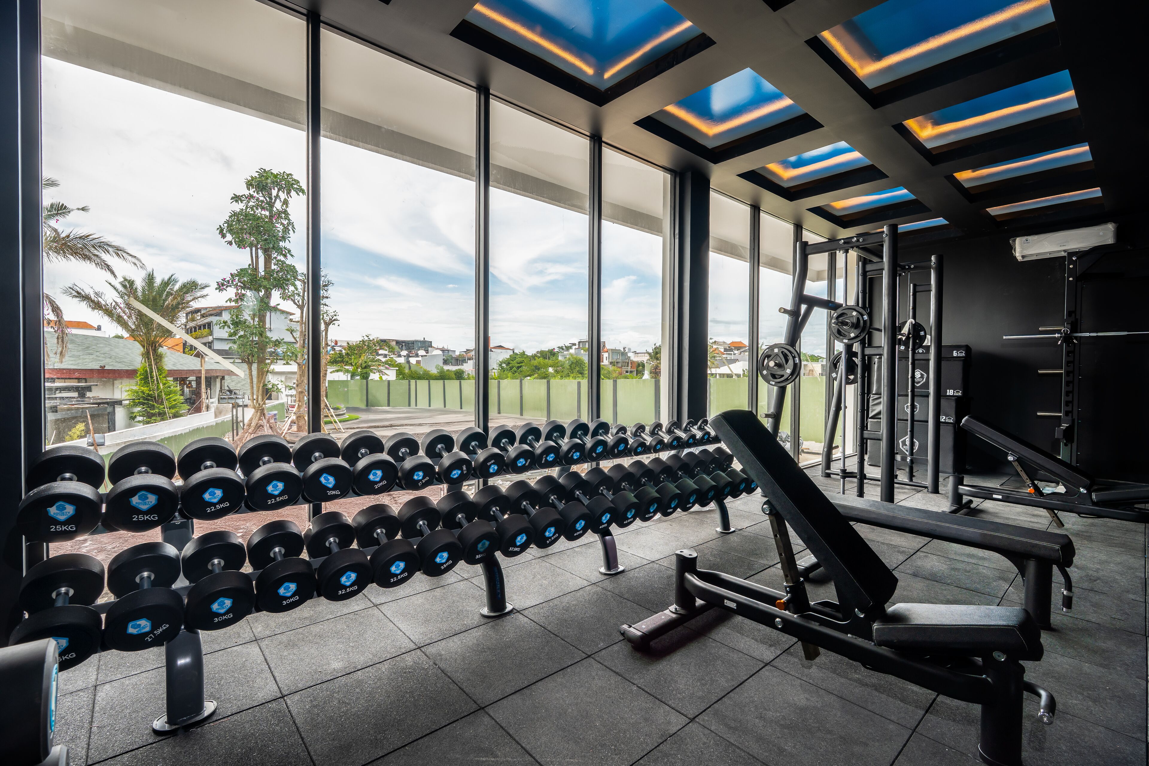 Ein Fitnessstudio mit einer Hantelbank, Kurzhanteln und Blick ins Freie.