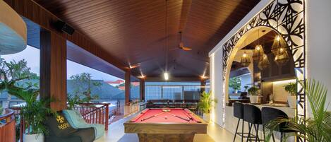 A pool table with surrounding seating, a bar area, and a view of the outdoors.