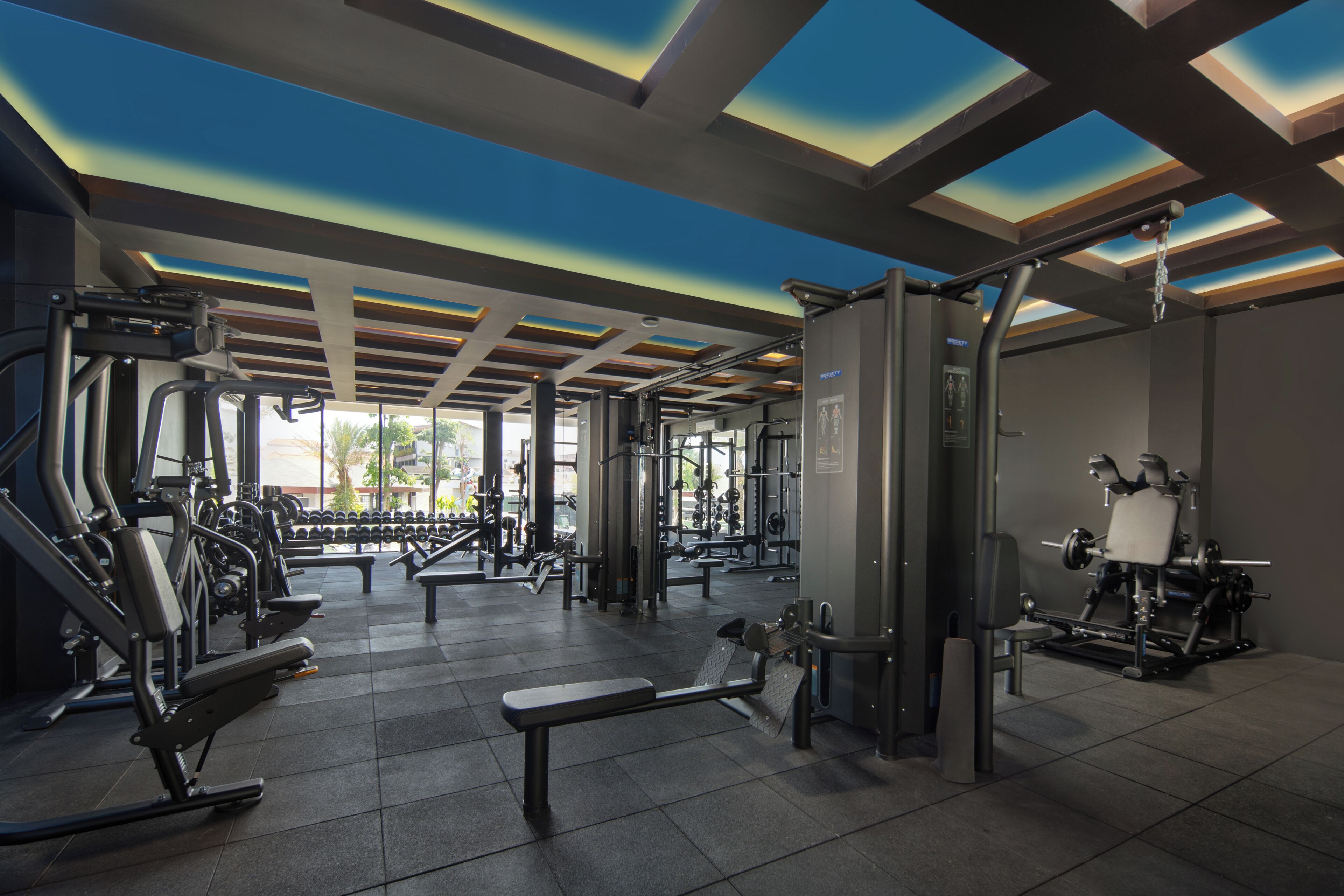 A gym with various exercise equipment, benches, and a ceiling with skylights.