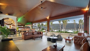 Un vaste espace intérieur doté d’un haut plafond, de canapés en cuir, d’une table basse en bois et offrant une vue sur les palmiers à l’extérieur.