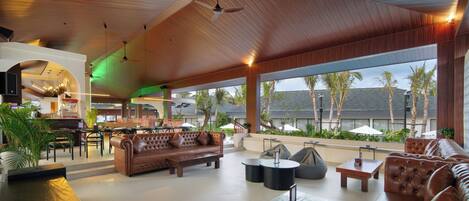 A spacious indoor area with a high ceiling, leather sofas, a wooden coffee table, and a view of palm trees outside.