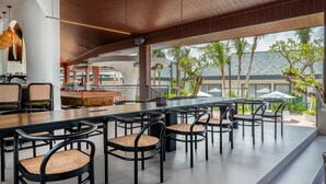 A modern outdoor dining area with a wooden ceiling, black chairs with woven seats, and a bar counter. - Maha Resort Bali (Canggu)