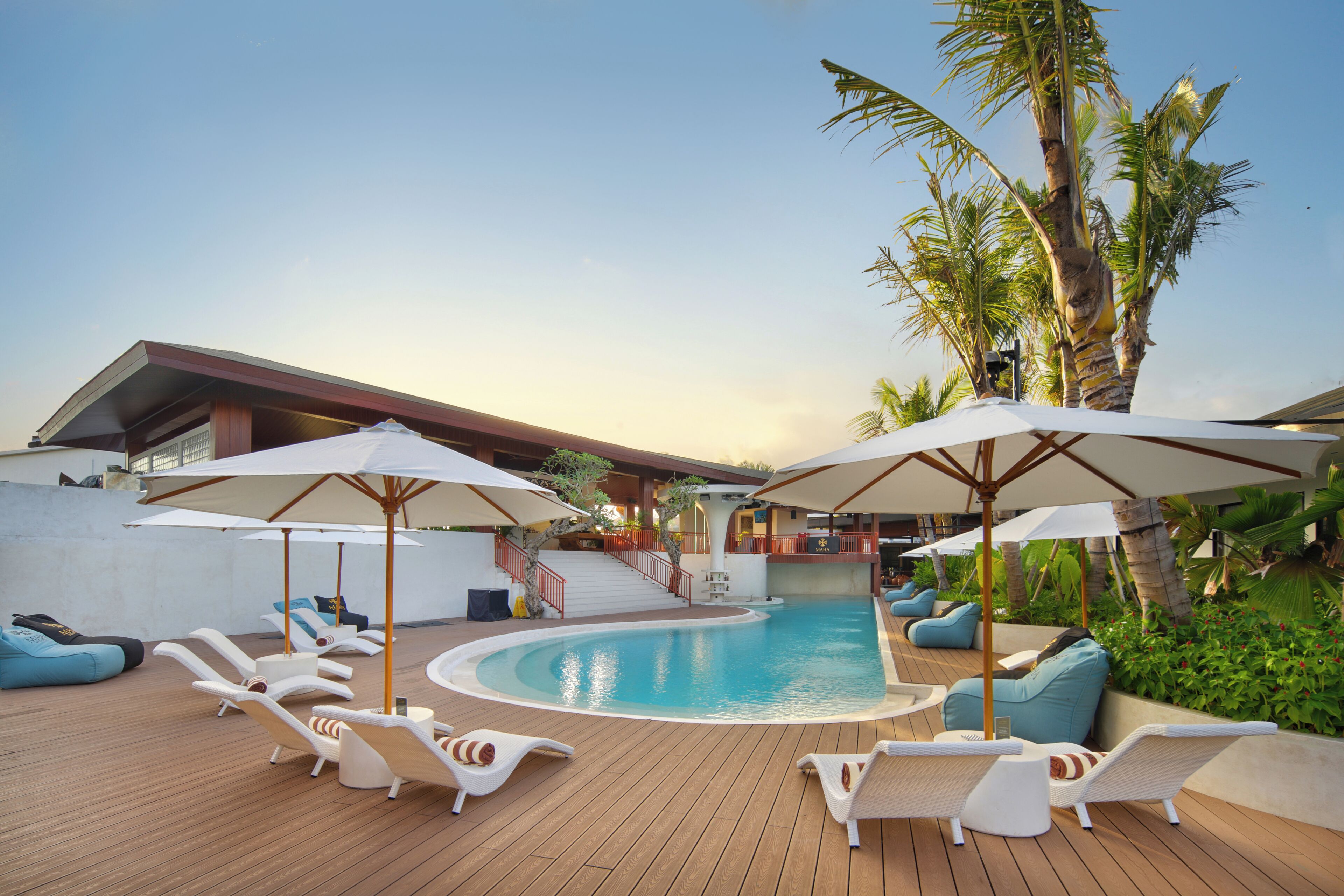 A pool area with lounge chairs, umbrellas, and a staircase leading to a deck.