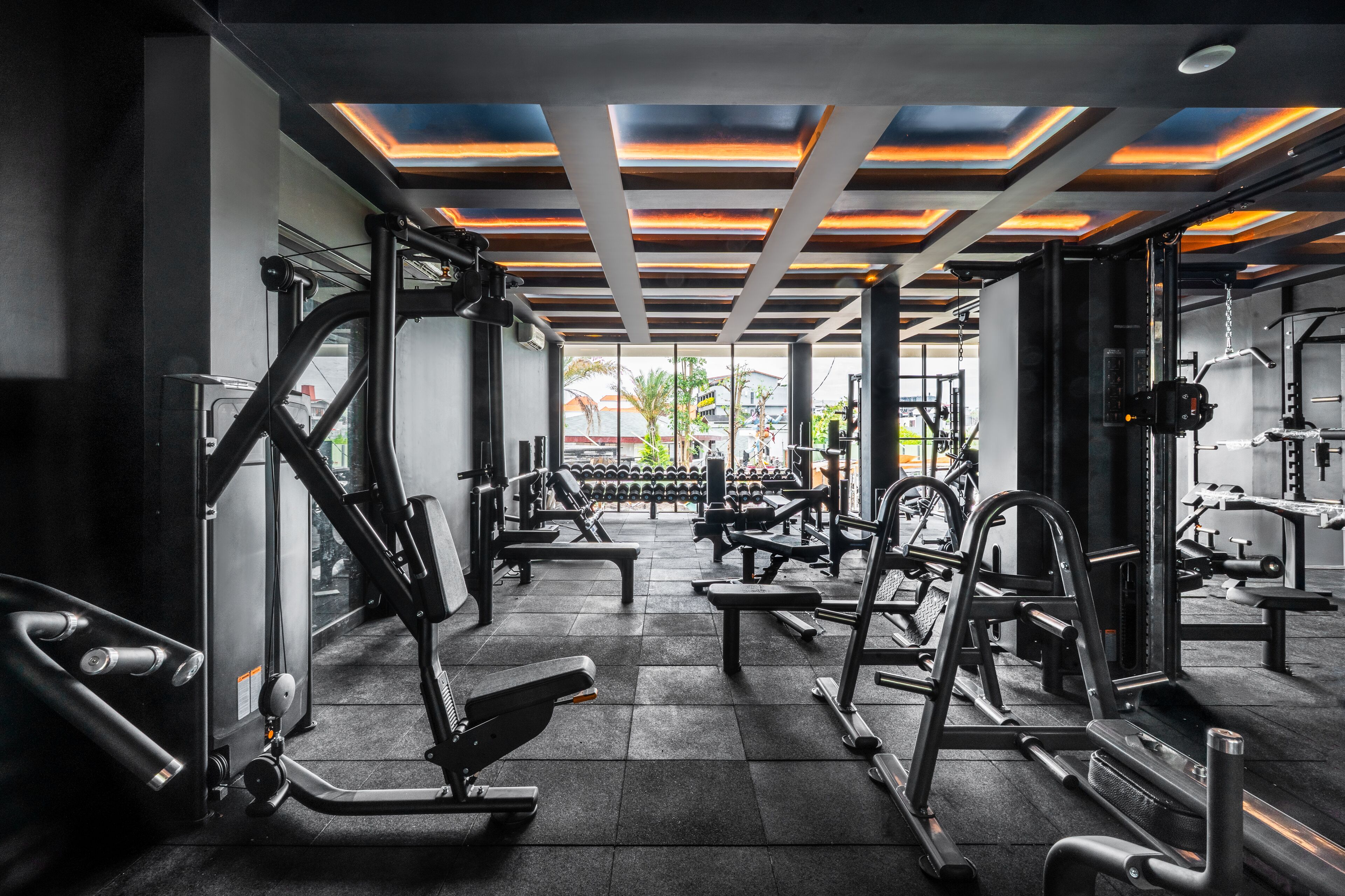 Un gimnasio con varios equipos de ejercicio, piso de baldosas y techo con un diseño geométrico.