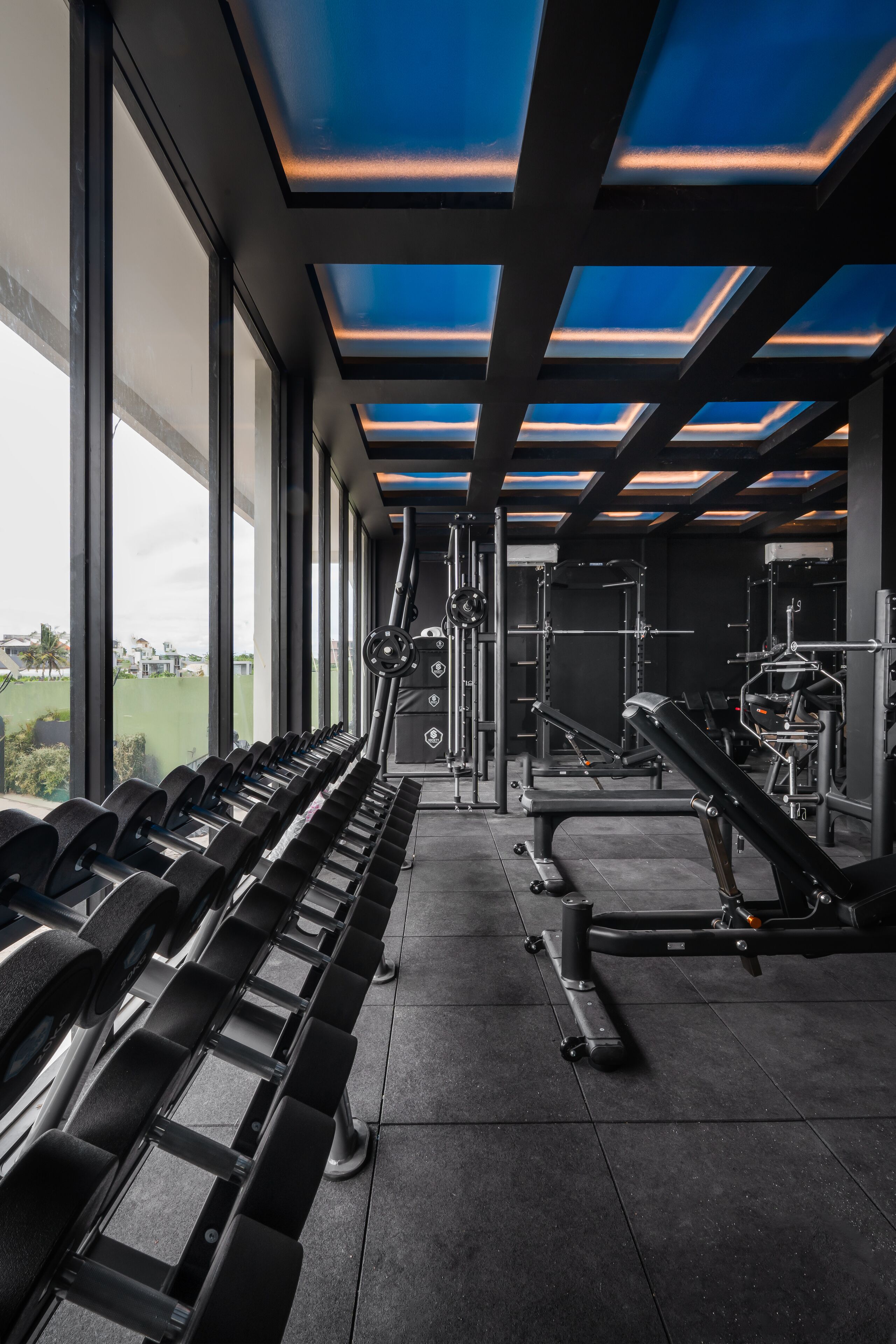 Une salle de sport équipée de matériel de musculation, de tapis de course et offrant une vue sur l’extérieur grâce à de grandes fenêtres.