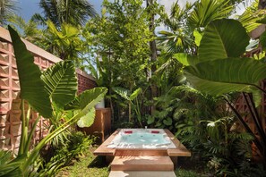 A hot tub surrounded by lush tropical plants and a wooden fence.