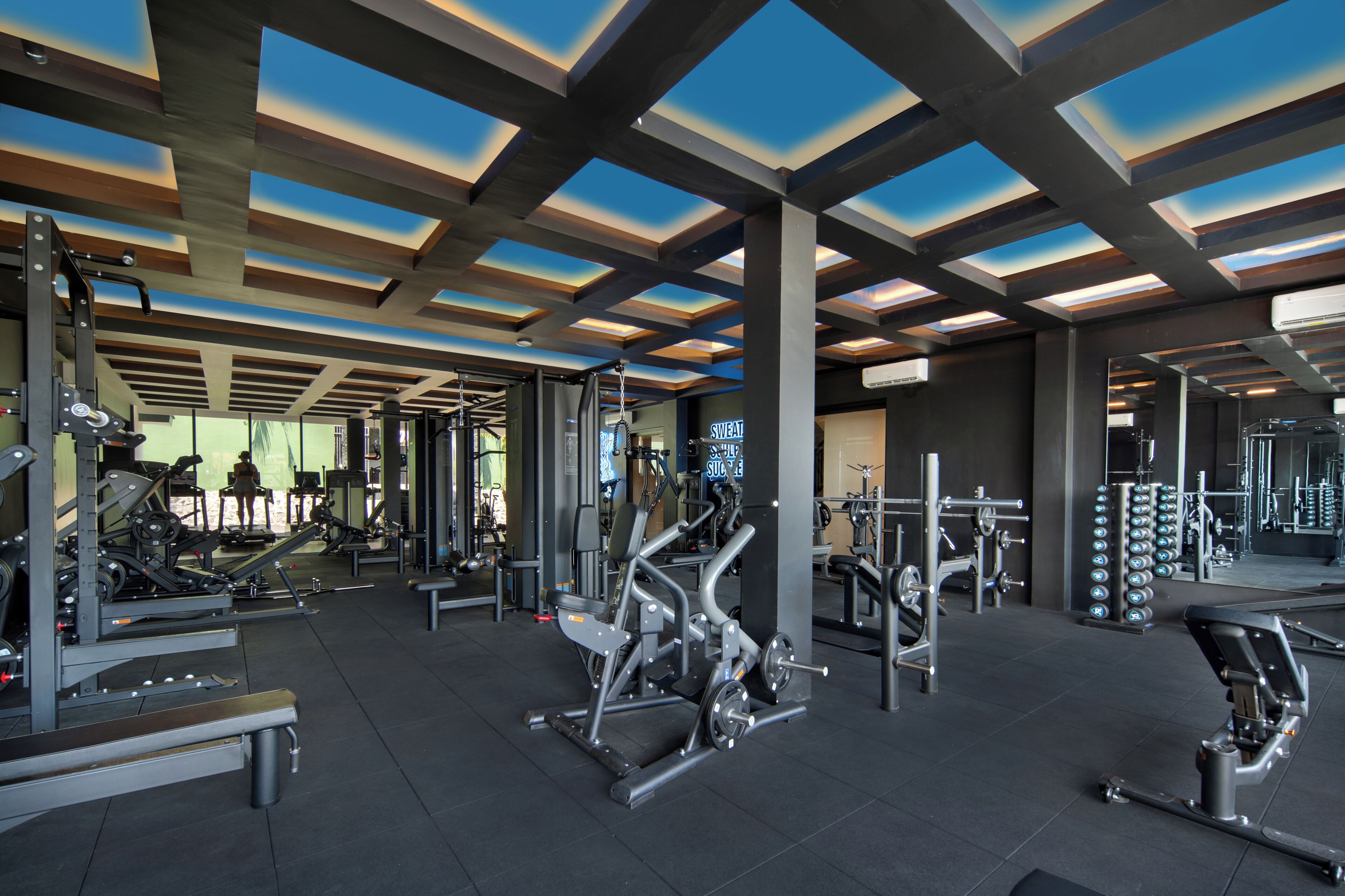 A gym with various exercise equipment, a mirrored wall, and a ceiling with skylights.