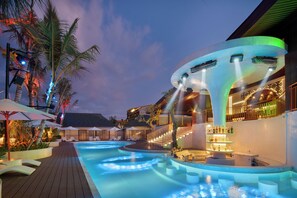 Un área de piscina con sillones de descanso, un bar y una escalera que lleva a un nivel superior.