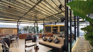 A covered outdoor seating area with sofas, tables, and chairs, overlooking a body of water. - Maha Resort Bali (Canggu)