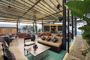 A covered outdoor seating area with sofas, tables, and chairs, overlooking a body of water. - Maha Resort Bali (Canggu)