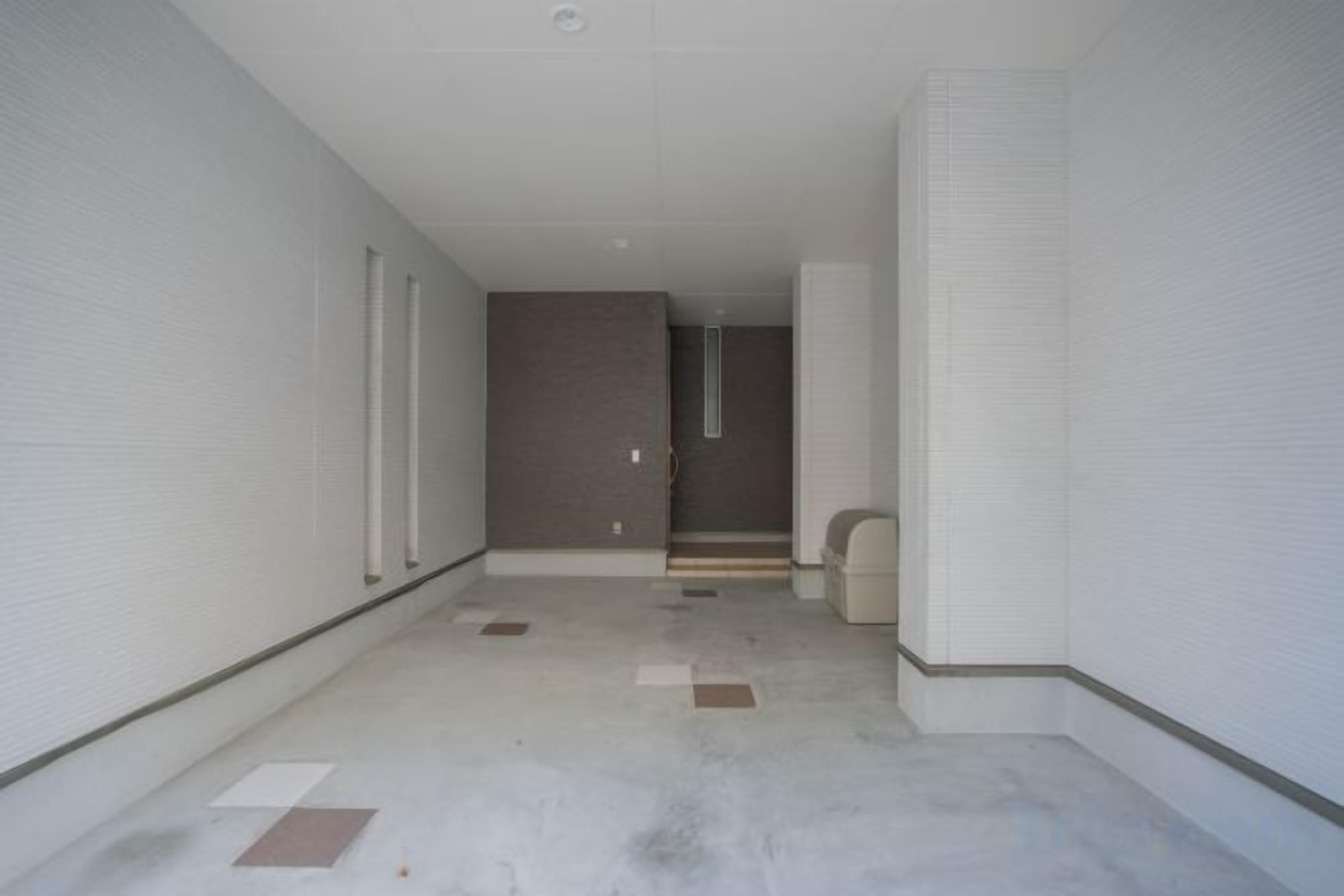 A corridor with white walls and a concrete floor, leading to a door with a window.