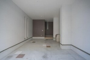 A corridor with white walls and a concrete floor, leading to a door with a window.